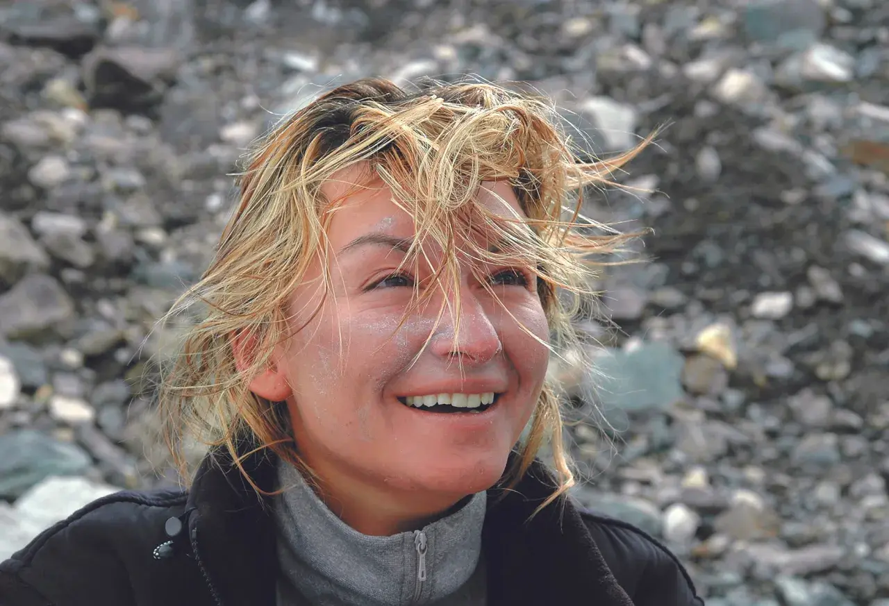 Martyna Wojciechowska z wiatrem we włosach, uśmiechnięta, na tle kamienistego zbocza. Może to być wspomnienie z wyprawy na Mount Everest.