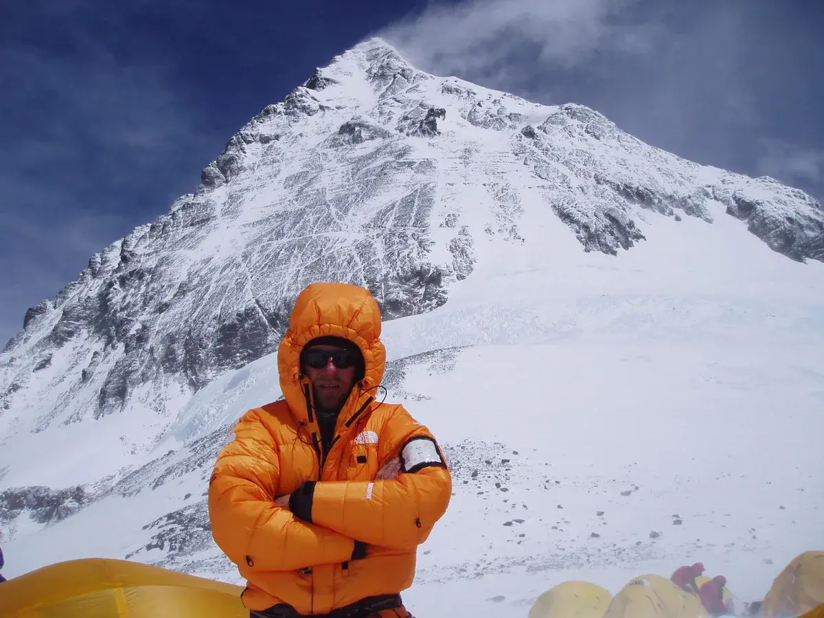 Alpinista w pomarańczowej kurtce na tle ośnieżonego szczytu. To może być jego wyczyn: mount everest bez tlenu.