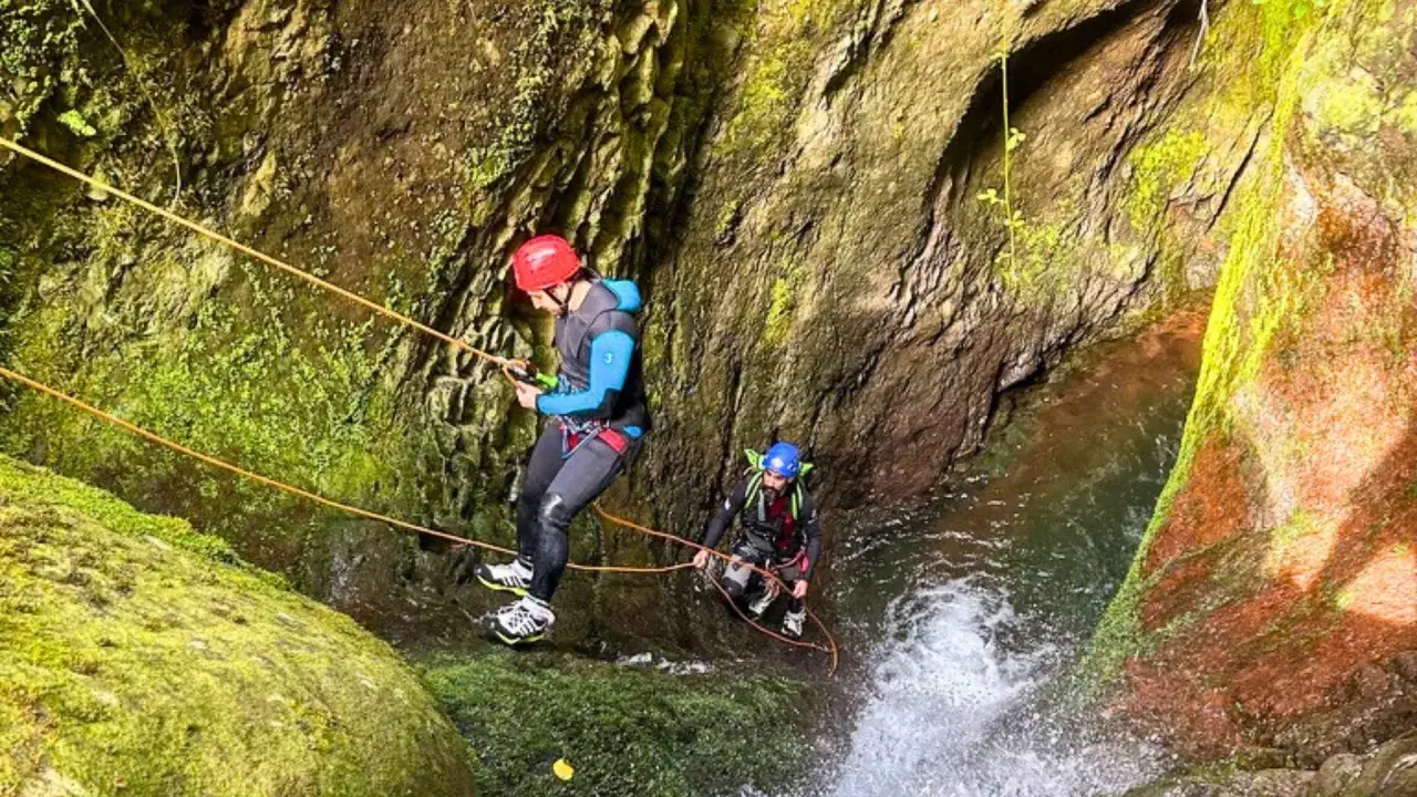 Dwóch mężczyzn w kaskach i piankach zjazdowych pokonuje wodospad w wąwozie. To właśnie jest canyoning!