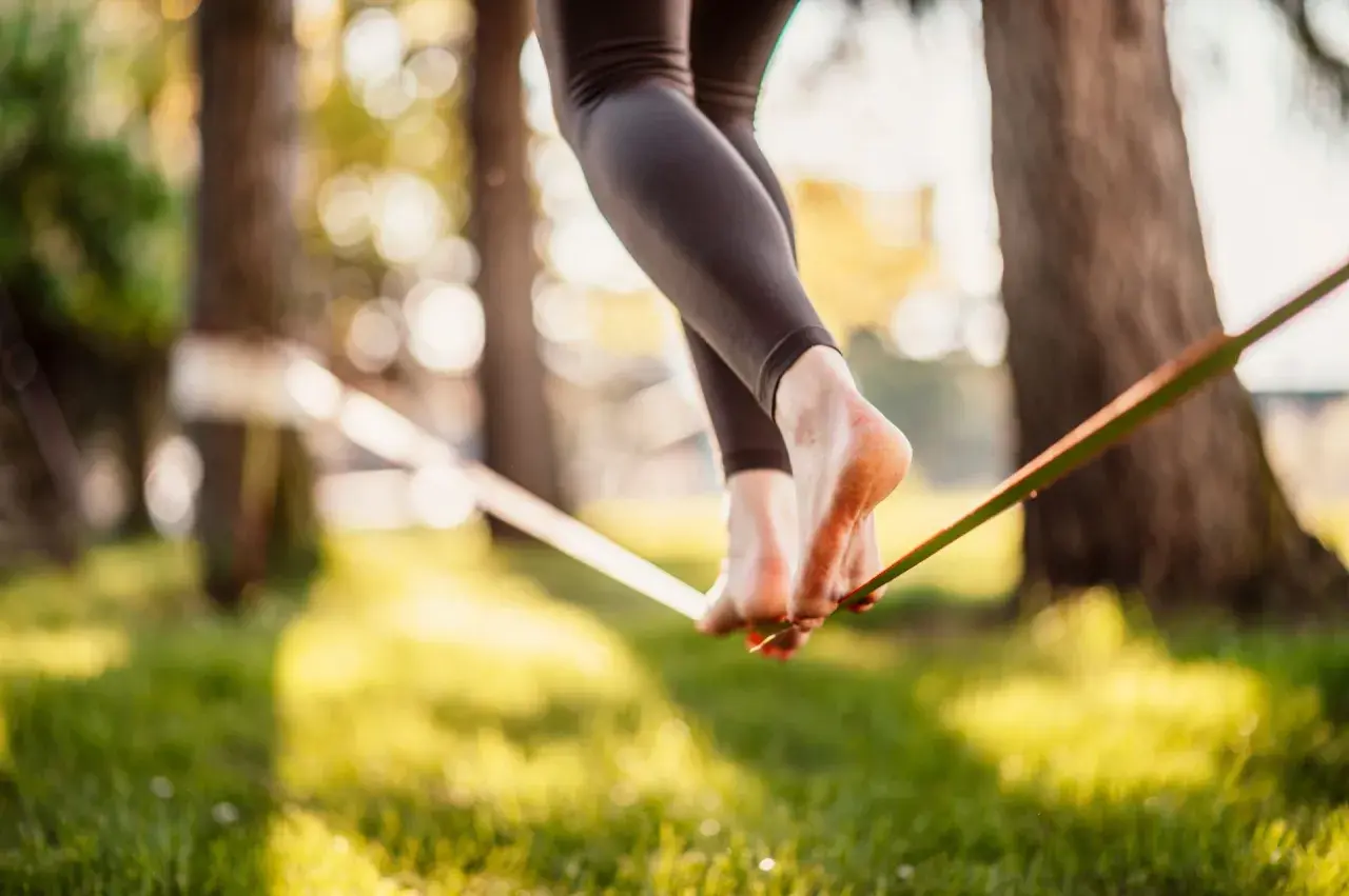 Chodzenie po taśmie to slackline. Widok na nogi balansujące na taśmie w parku, w promieniach słońca.