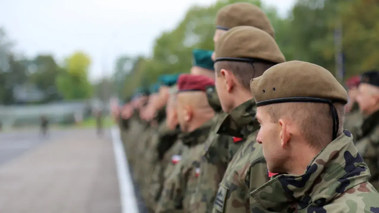 Żołnierze w kamuflażu i beretach stoją w szeregu. To kategoria d wojsko.