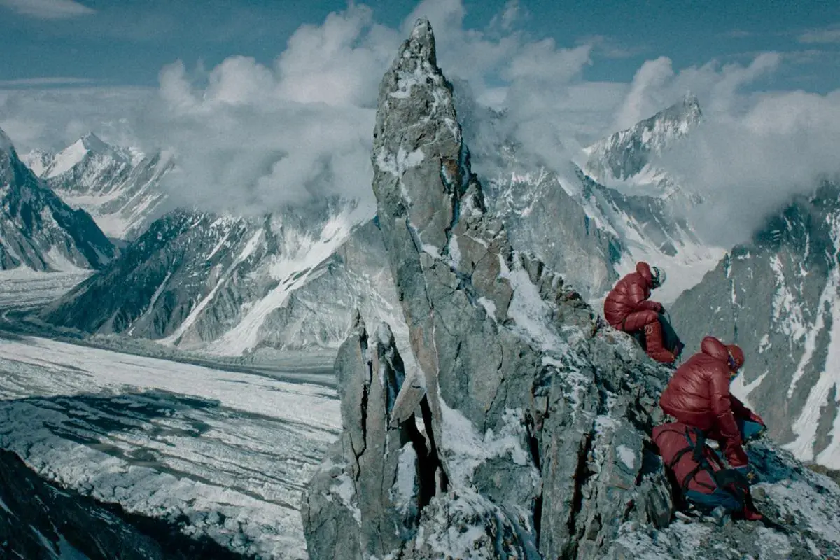 Wyprawa na Broad Peak 2013. Dwóch wspinaczy w czerwonych kurtkach odpoczywa na skalistym zboczu, podziwiając lodowce i ośnieżone szczyty.