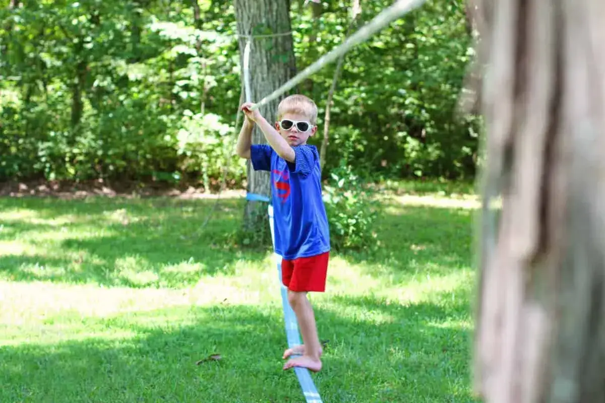 Chłopiec w okularach przeciwsłonecznych balansuje na taśmie, ćwicząc slackline. To świetna zabawa i trening równowagi!