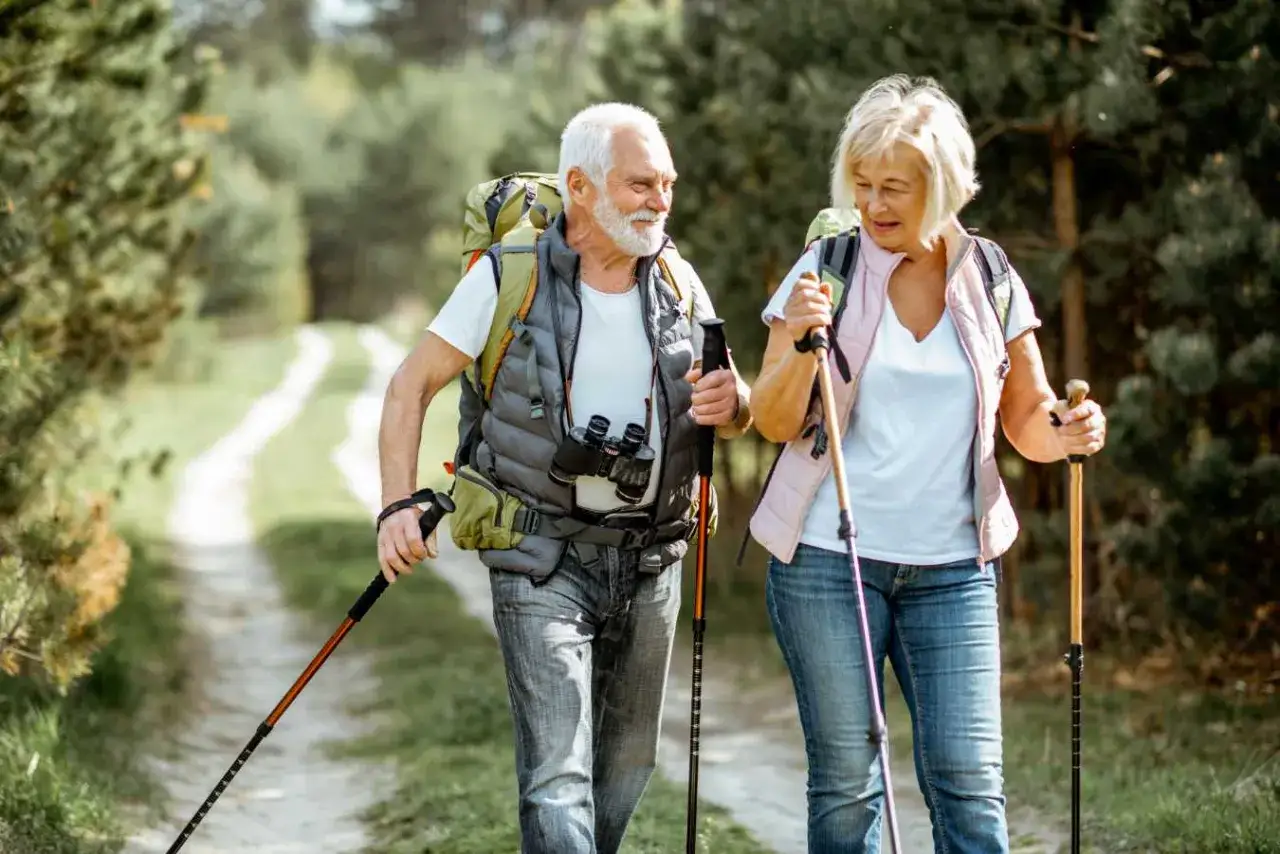Starsza para z plecakami i kijkami trekkingowymi na leśnej ścieżce. Pokazują, jak chodzić z kijkami trekkingowymi, czerpiąc radość z natury.