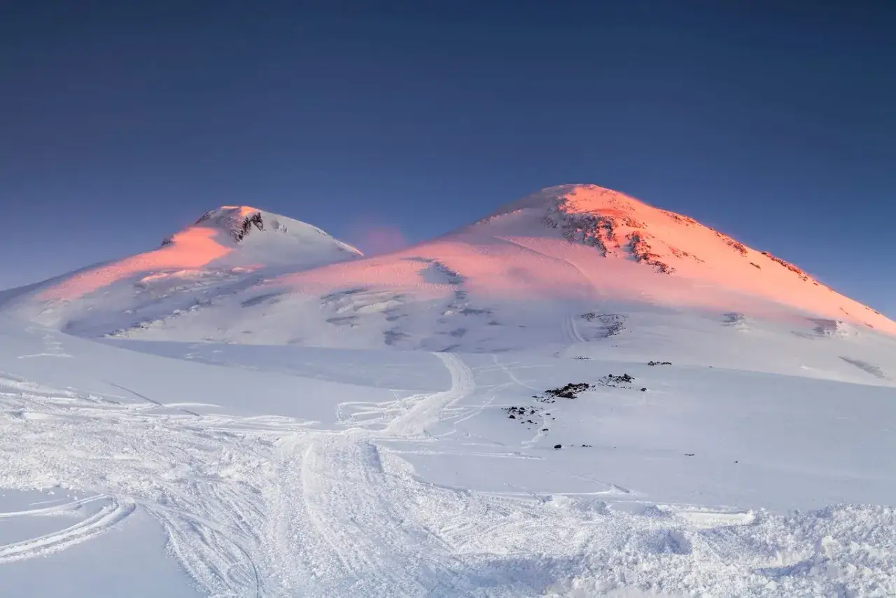 Elbrus, najwyższy szczyt w Europie, skąpany w różowym blasku wschodzącego słońca. Śnieżne zbocza usiane śladami nart.