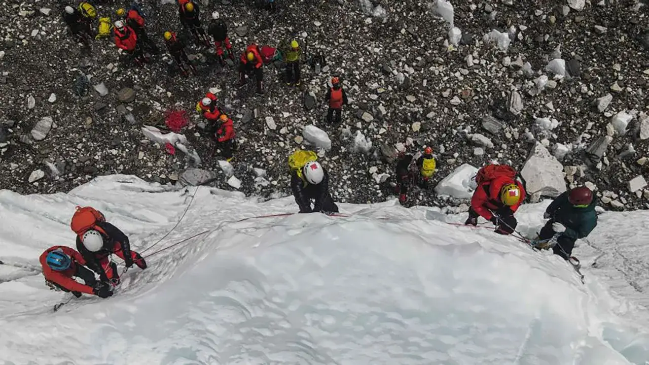Wspinacze pokonują lodospad na Everest. Grupa ludzi w kolorowych kurtkach i kaskach, zabezpieczona linami, wspina się po ośnieżonym zboczu.