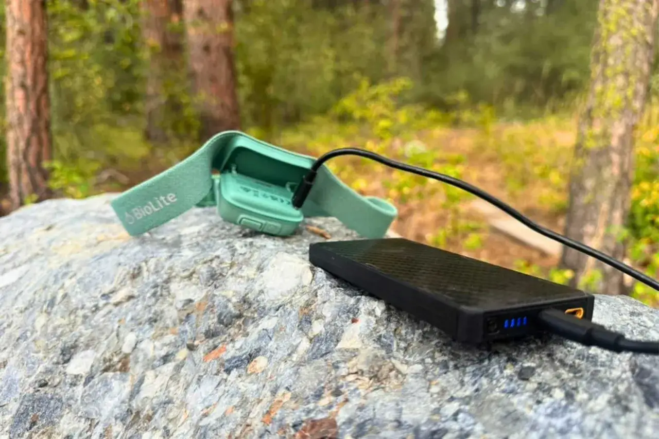 Zielona lampka czołowa BioLite ładuje się z czarnego powerbanku na kamieniu. Wskazuje to, jak długo ładuje się powerbank, gdy jesteś na łonie natury.