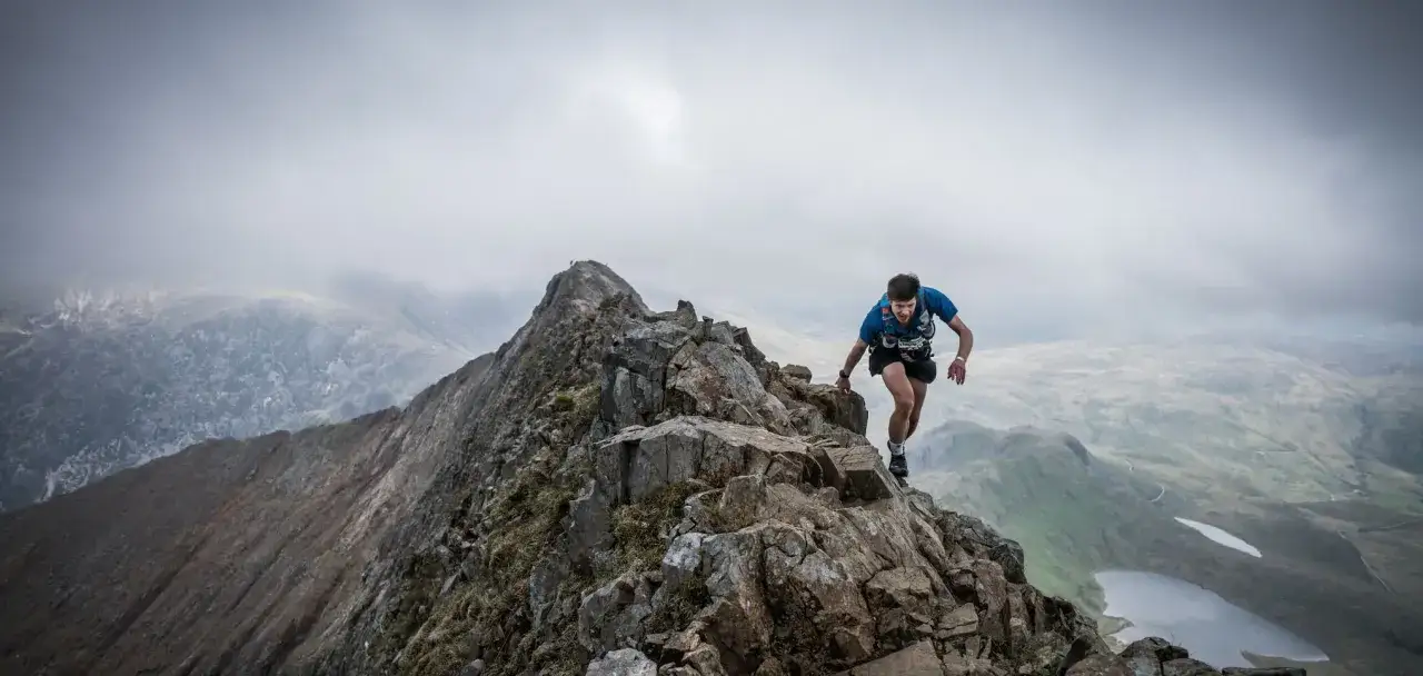 Biegacz pokonuje skalisty grzbiet, walcząc z żywiołem. To obraz z Barkley Marathon, gdzie każdy krok to wyzwanie.