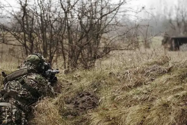 Gracz w kamuflażu leży w okopie, celując z repliki broni. Idealne miejsce, gdzie można strzelać z ASG, wśród zarośli i suchej trawy.