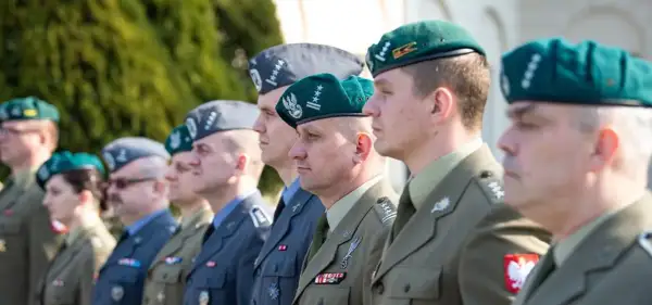Żołnierze w różnych rodzajach mundurów wojskowych, w tym w zielonych beretach i szarych furażerkach, prezentują swoje odznaczenia i stopnie wojskowe.