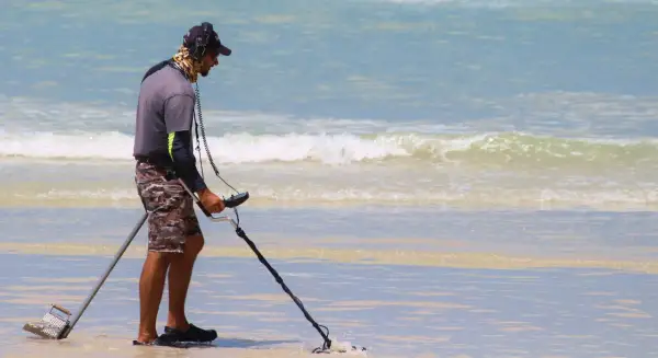 Mężczyzna z wykrywaczem metali na plaży. Czy wykrywacz metali jest legalny? Szuka skarbów w wodzie.