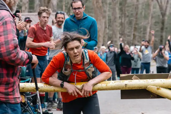 Zmęczona biegaczka opiera się o barierkę podczas Barkley Marathon. Tłum kibicuje, widząc jej determinację.
