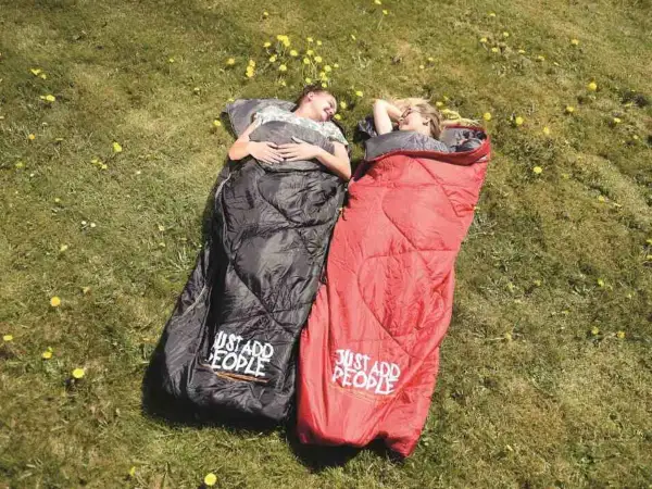 Dwie osoby leżą w śpiworach na trawie. Czarny śpiwór lewy czy prawy? Czerwony śpiwór też.