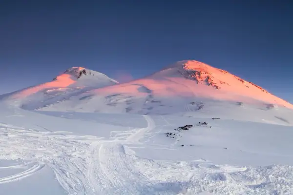 Elbrus, najwyższy szczyt w Europie, skąpany w różowym świetle wschodu słońca. Śnieżne zbocza usiane śladami nart.