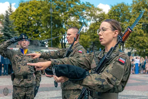 Żołnierze w mundurach polowych, z karabinami, przygotowują się do przysięgi wojskowej. To ważny moment, jak się ubrać na przysięgę wojskową? Mundur to podstawa.