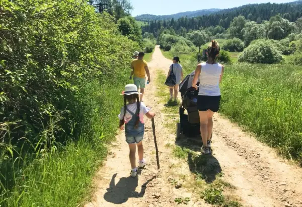 Rodzina spaceruje po górskiej ścieżce w Beskidach. Dziecko z patykiem idzie przodem, a za nim rodzice z wózkiem.
