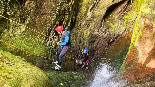 Dwóch mężczyzn w kaskach i piankach zjazdowych pokonuje wodospad w wąwozie. To właśnie jest canyoning!