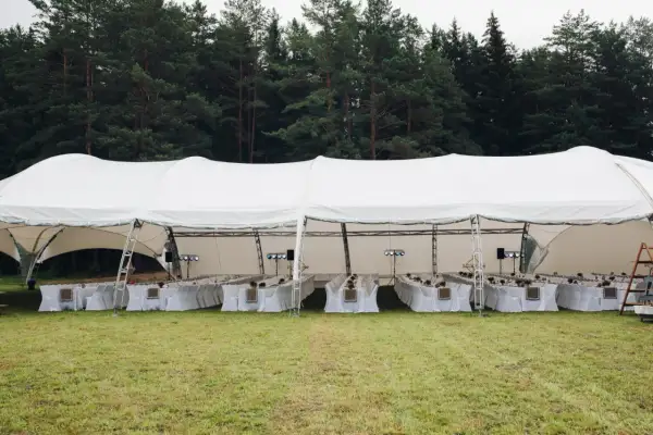 Duży biały namiot weselny z długimi stołami i krzesłami, gotowy na przyjęcie. Jak rozłożyć namiot? To proste, gdy masz taką konstrukcję!